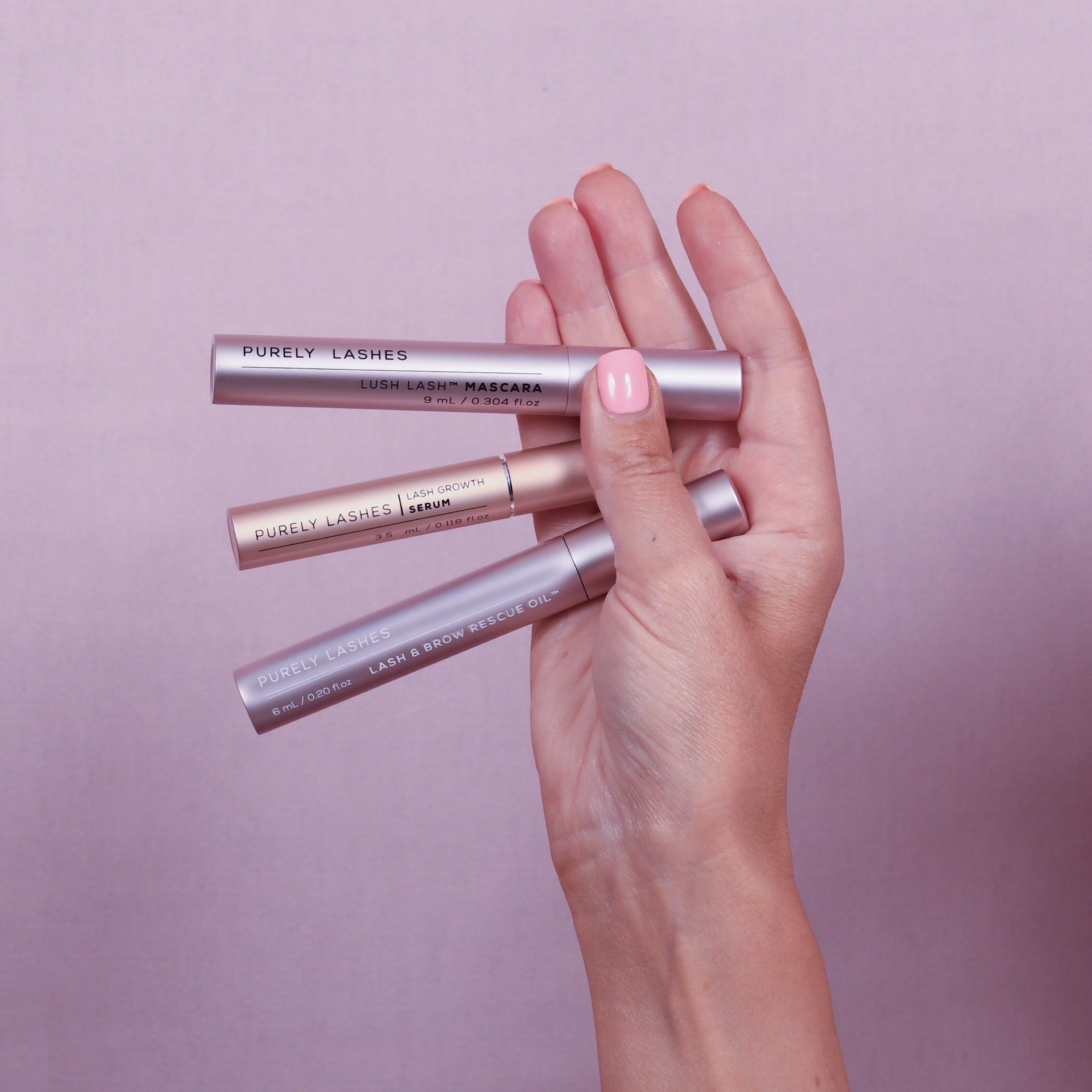 hand with painted nails holding three products. Growth Mascara, Lash Growth Serum, Lash and Brow Rescue Oil