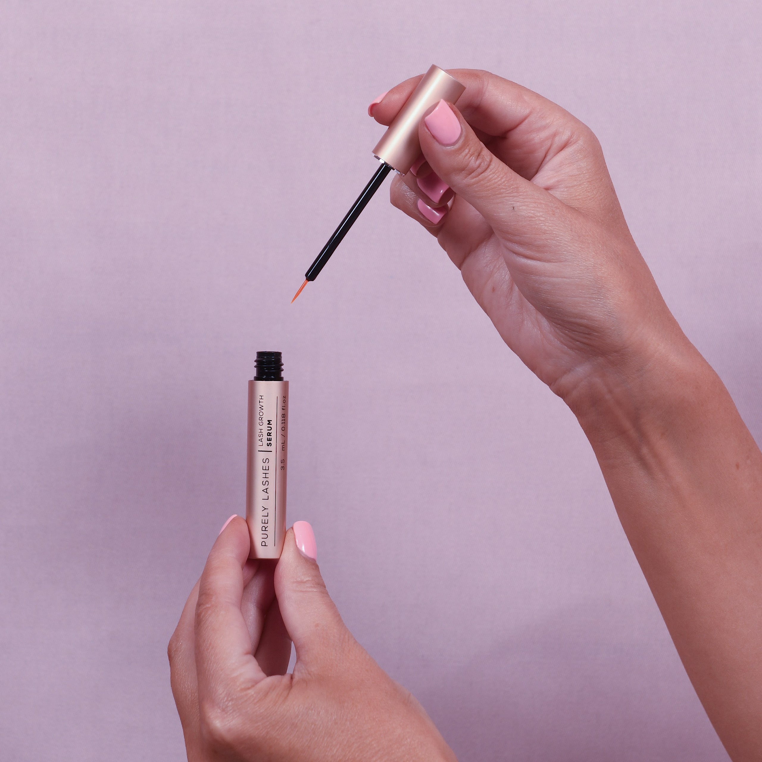 Womans hand raising the applicator from the vile of lash growth serum