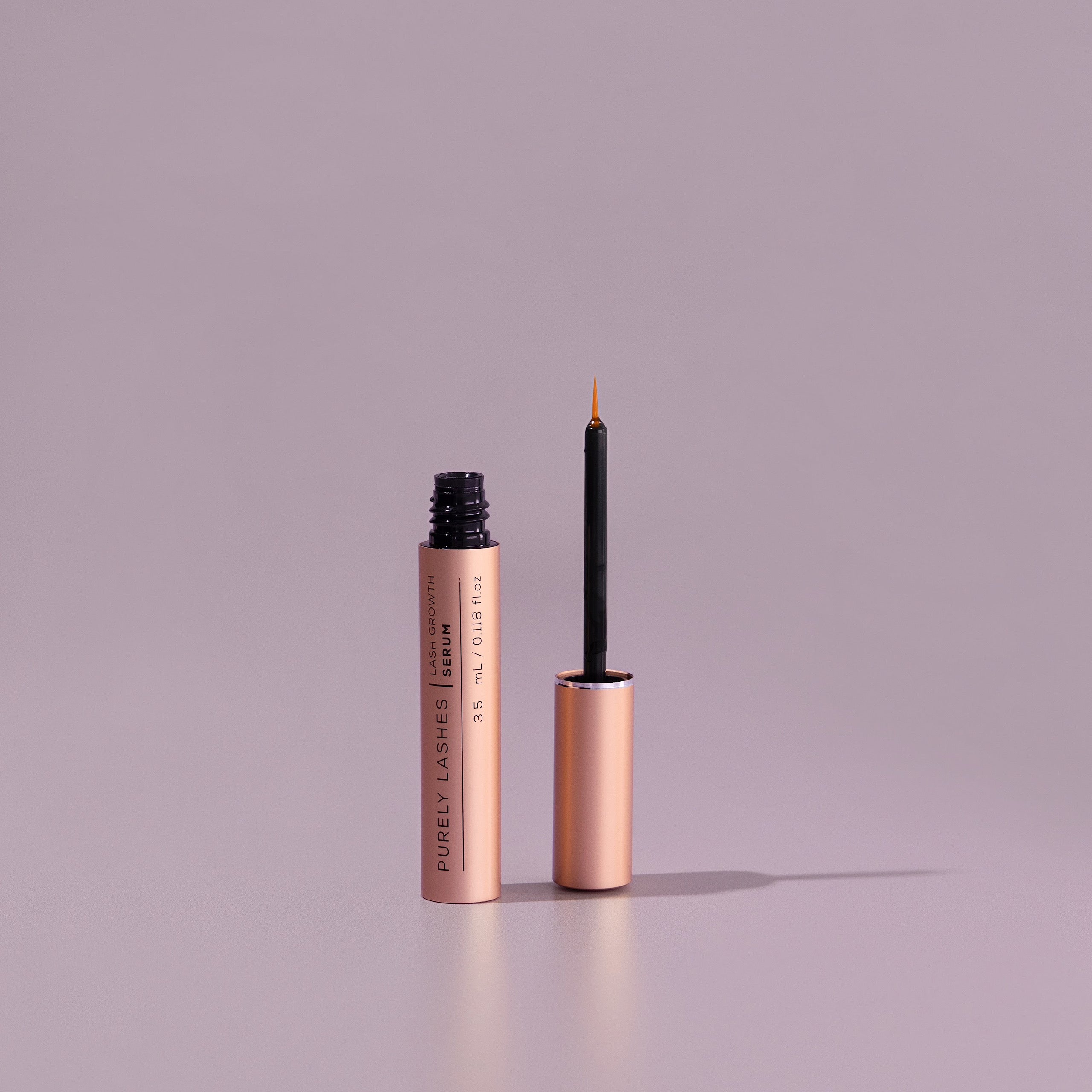 Uncapped bottle of lash growth serum beside upturned applicator which is the viles cap